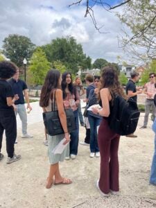 Four students stand in a circle eating bagels and talking