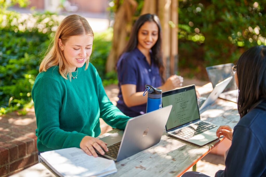 Two students working together on laptops at a table outside.