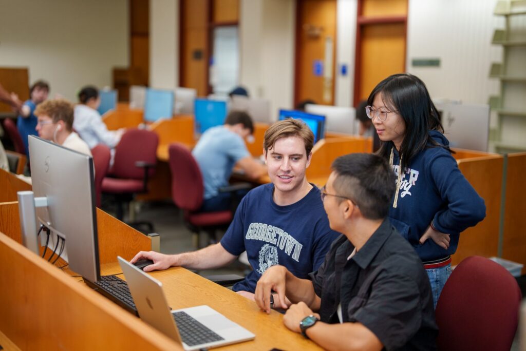 Three students working together at a computer in the library.