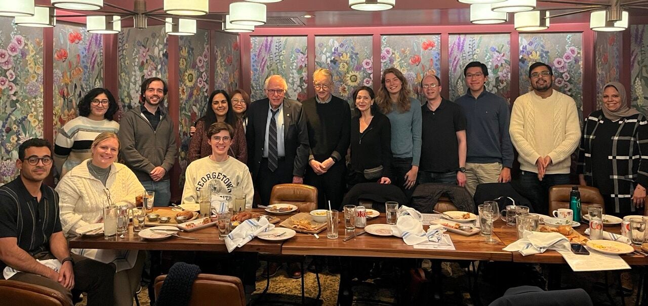 A group poses with Senator Sanders and Professor Hinton in front of dinner table
